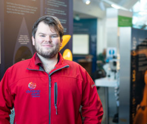 2017 SAMS UHI alumni Blair Watson poses for the camera in his red Dynamic Earth uniform jacket whilst on a recent work trip back to his old uni campus at SAMS UHI in Oban.