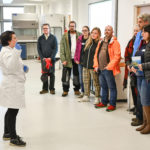 Student ambassador Darcie wearing lab coat talks to a group of Open Day attendees about some of the undergrad practical sessions in the main teaching lab at SAMS that students can expect on the BSc programme.