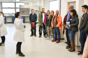 Student ambassador Darcie wearing lab coat talks to a group of Open Day attendees about some of the undergrad practical sessions in the main teaching lab at SAMS that students can expect on the BSc programme.