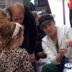 Artemis (far right) in lab coat talks to 2 young girls about how the ocean can be monitored from space at a recent "Our World From Space" outreach event.