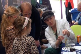 Artemis (far right) in lab coat talks to 2 young girls about how the ocean can be monitored from space at a recent "Our World From Space" outreach event.