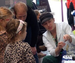 Artemis (far right) in lab coat talks to 2 young girls about how the ocean can be monitored from space at a recent "Our World From Space" outreach event.